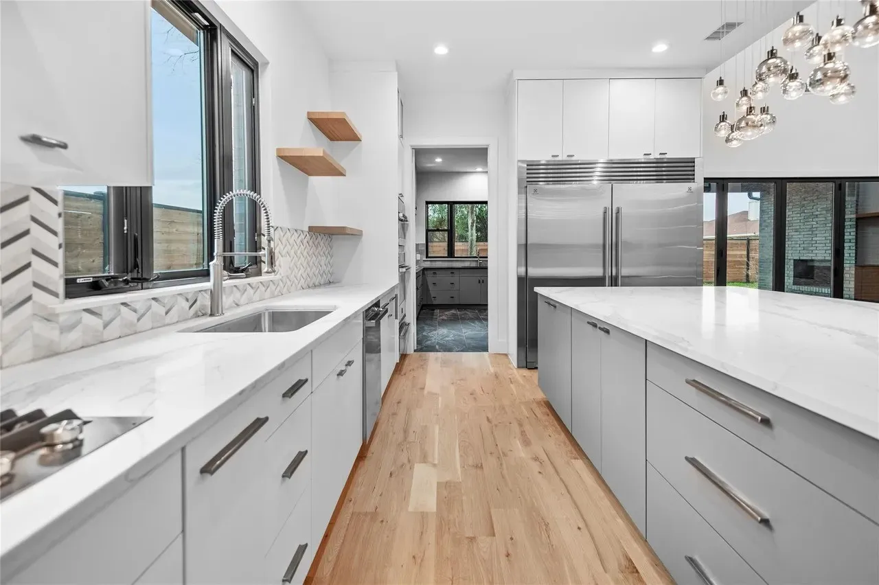 Modern kitchen featuring light wood-finish flooring, white upper cabinetry, and a large island with a light-colored countertop