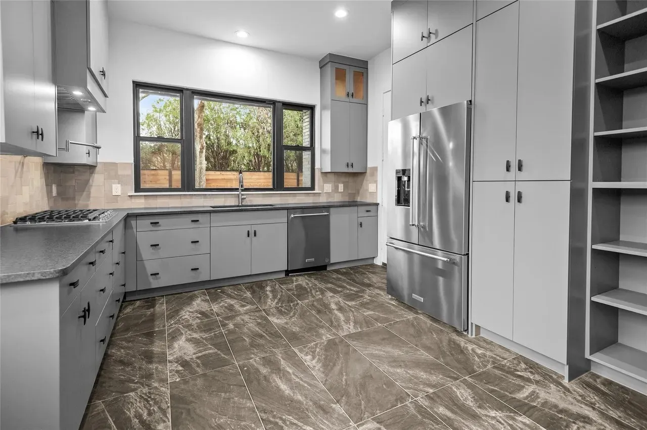 Modern kitchen featuring grey cabinetry, dark marble-finish flooring, and a large multi-pane window