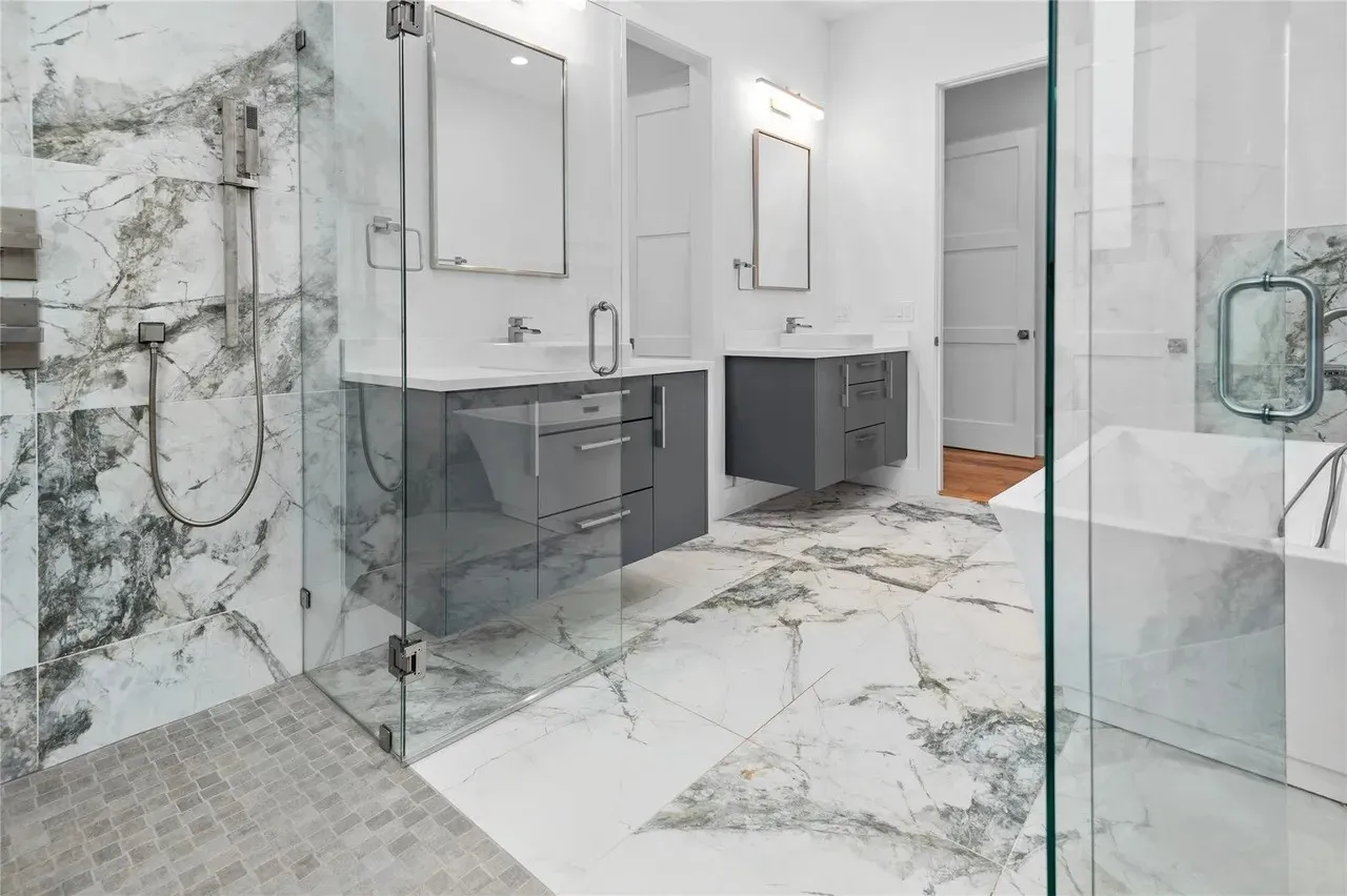 Modern bathroom featuring a glass-enclosed shower with a mosaic tile floor, a freestanding soaking tub, and a dual vanity with grey cabinetry
