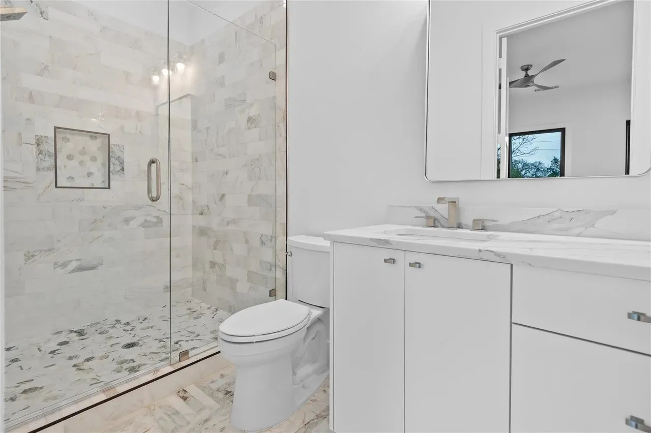 Bathroom featuring a glass-enclosed shower with tiled walls and floor, a white vanity with a countertop, a rectangular mirror, and a modern toilet
