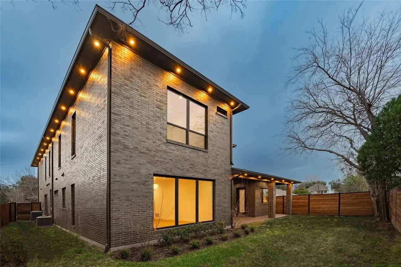 Contemporary brick exterior with large windows, recessed soffit lighting, a covered patio, and wood fencing