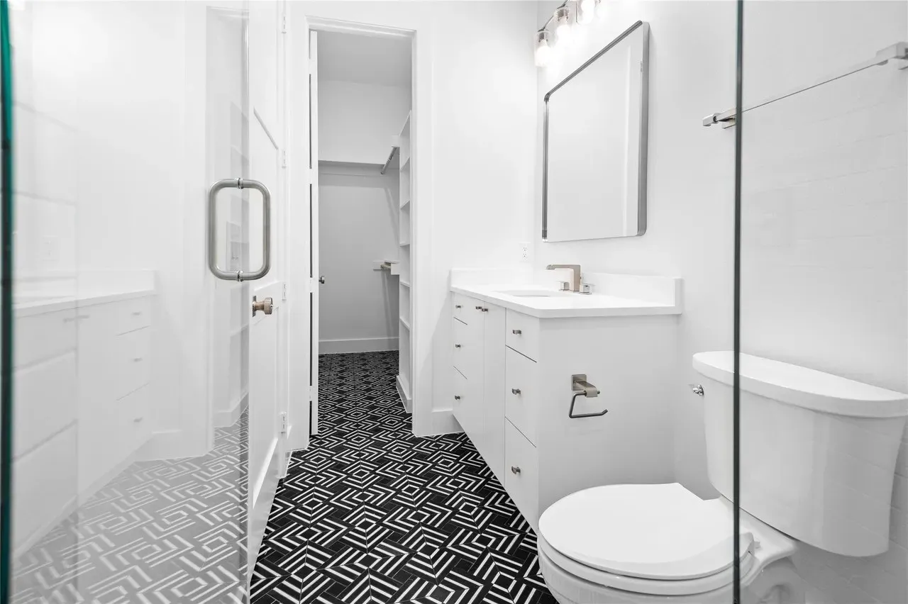 Modern bathroom featuring black and white patterned floor tile, white vanity with integrated sink, rectangular framed mirror, and glass shower​​‌​​​​‌​​‌‌​‌‌​​​‌‌​‌​‌​‌​​​‌​​ enclosure