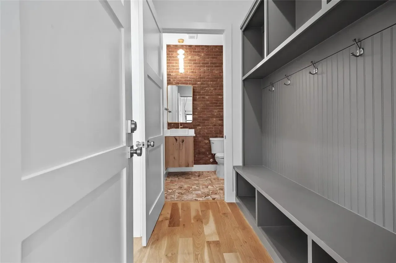 Mudroom featuring built-in gray cabinetry with bench seating, wall hooks, and overhead storage