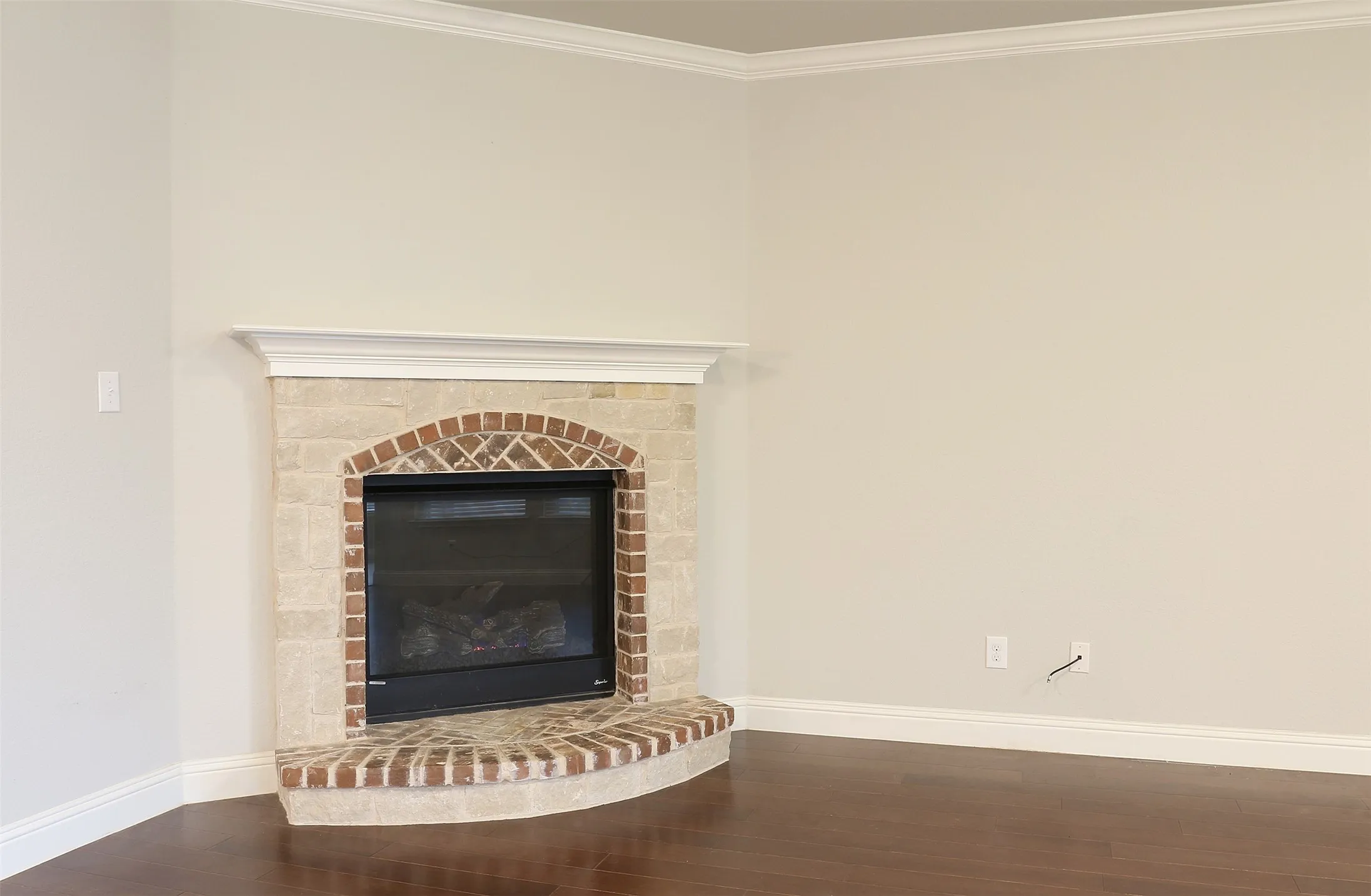 Corner fireplace featuring a brick hearth and stone surround with a decorative wood mantel