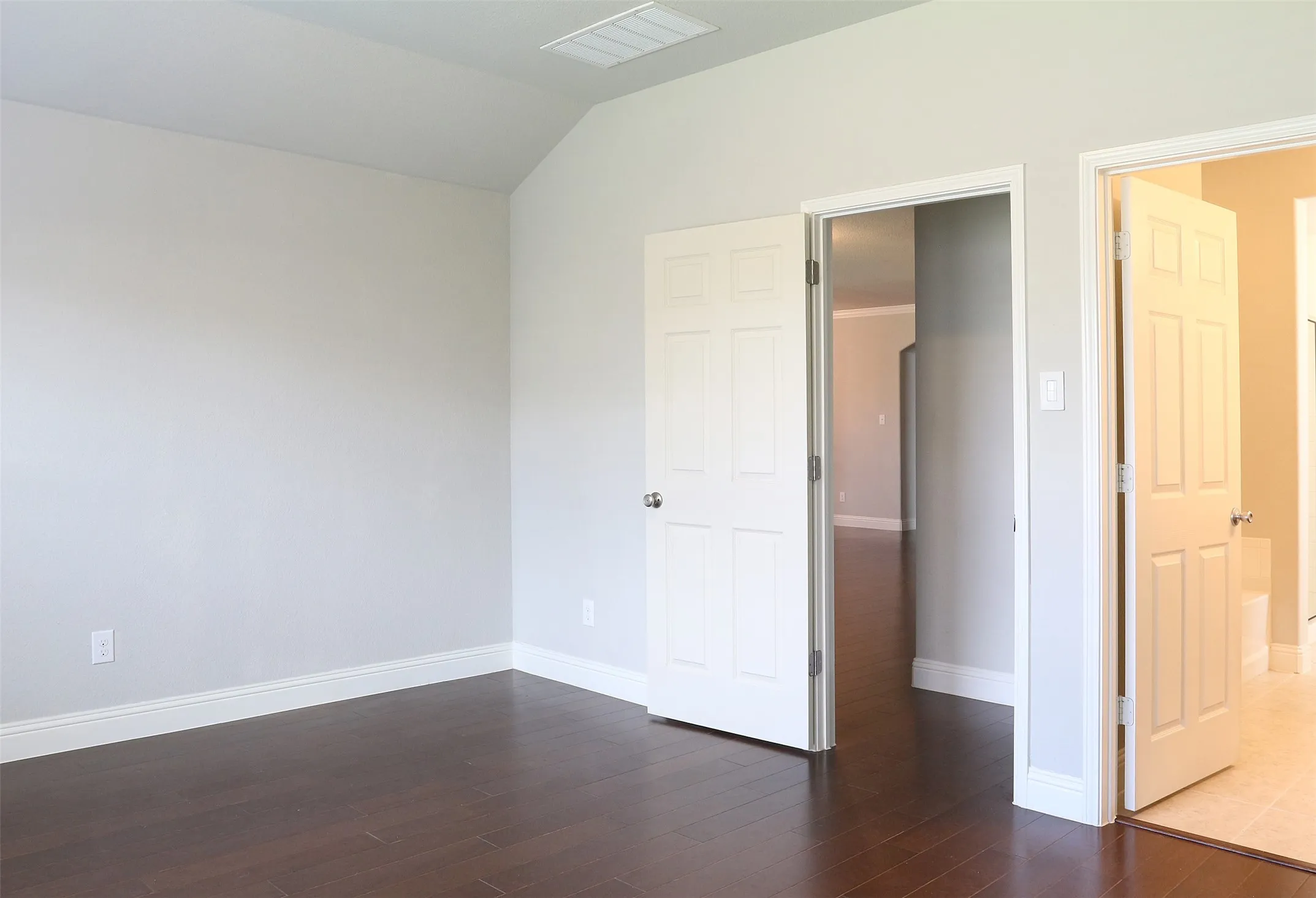 Interior room featuring wood-finish flooring, light gray wall paint, white baseboards, and two white panel doors