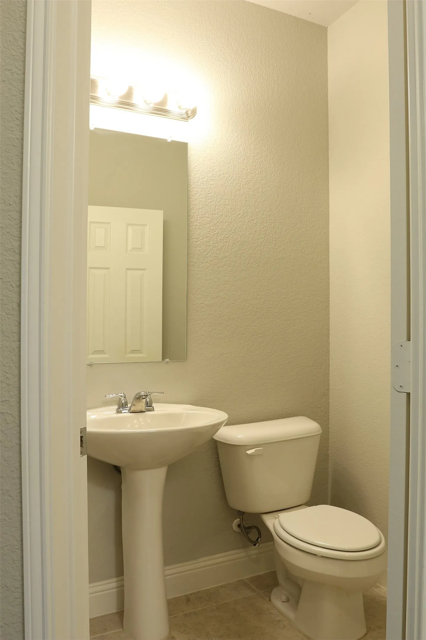 Pedestal sink with chrome faucet, toilet, and vanity lighting fixture