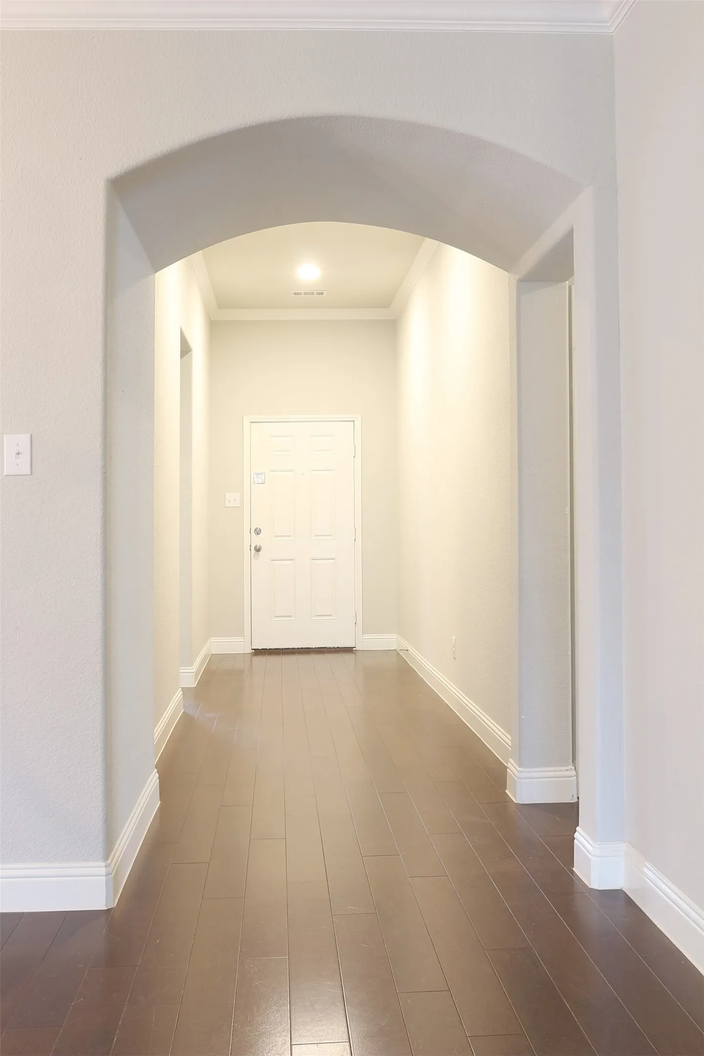 Arched entryway opening to a hallway with wood-finish flooring, white baseboards, and crown molding