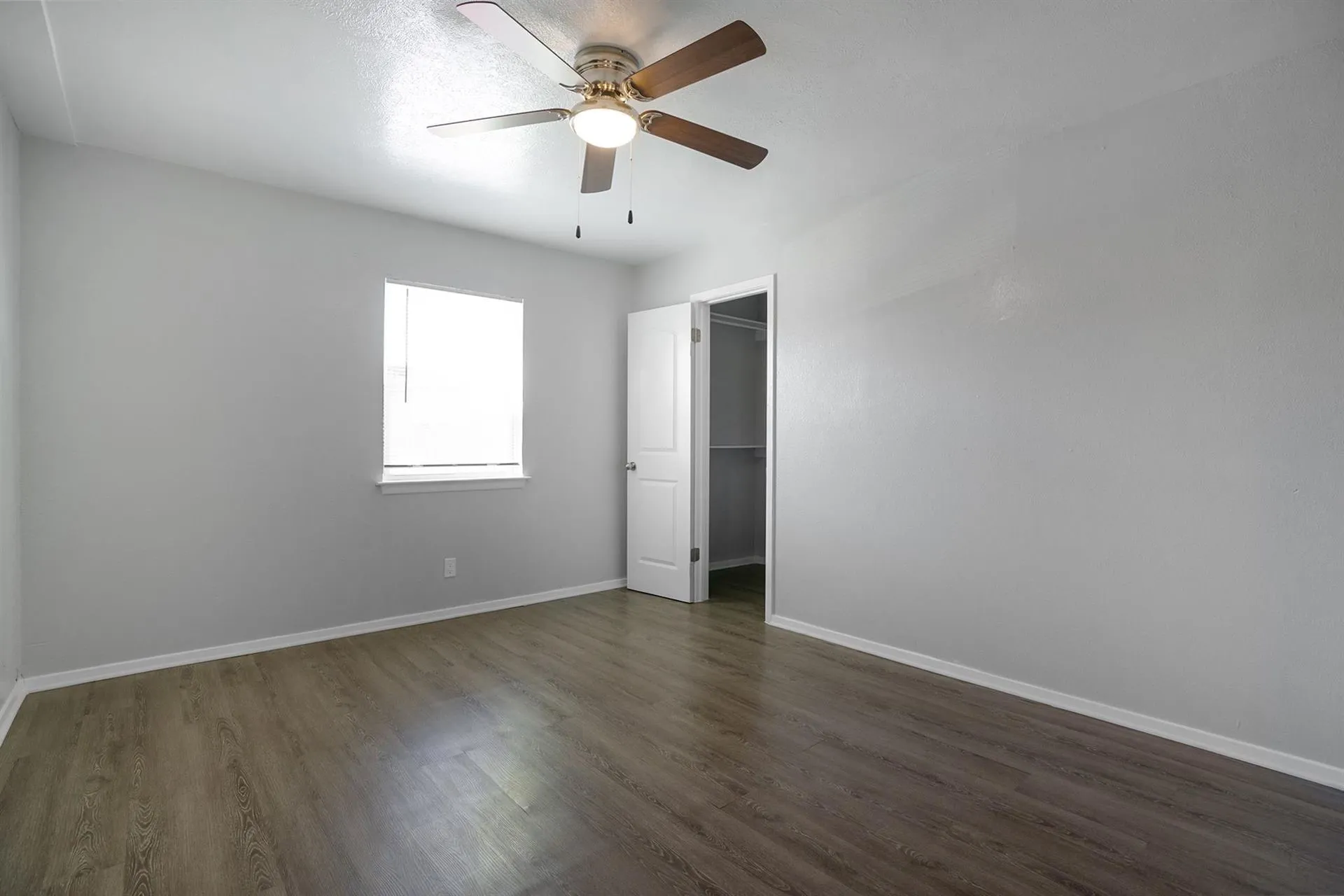Room featuring wood-finish flooring, light gray walls, a ceiling fan with integrated lighting, a single window with blinds, and a closet with shelving