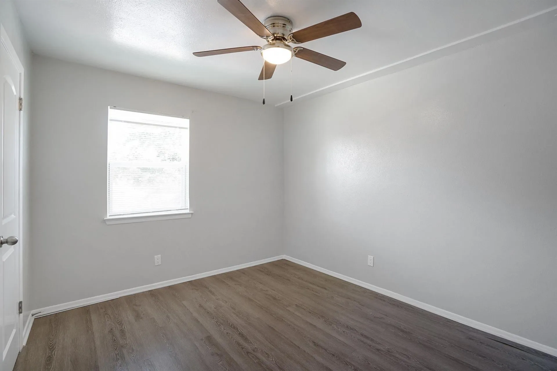 Room featuring wood-finish flooring, a ceiling fan with integrated lighting, and a window with blinds