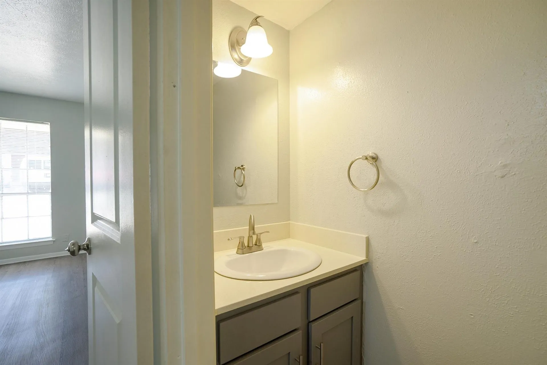Bathroom vanity with a white countertop and integrated sink, brushed nickel faucet, and a wall-mounted light fixture
