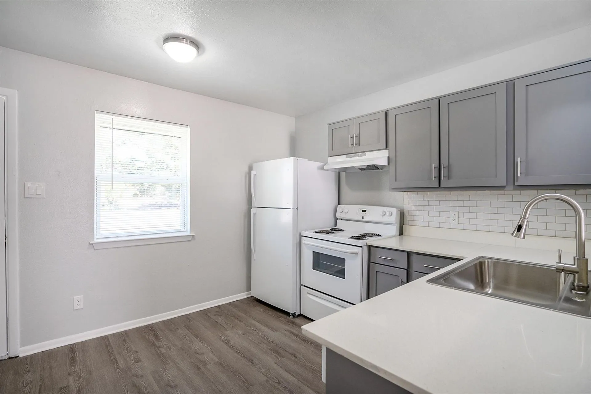 Kitchen featuring gray cabinetry, white countertops, white subway tile backsplash, stainless steel sink with gooseneck faucet, and wood-finish flooring
