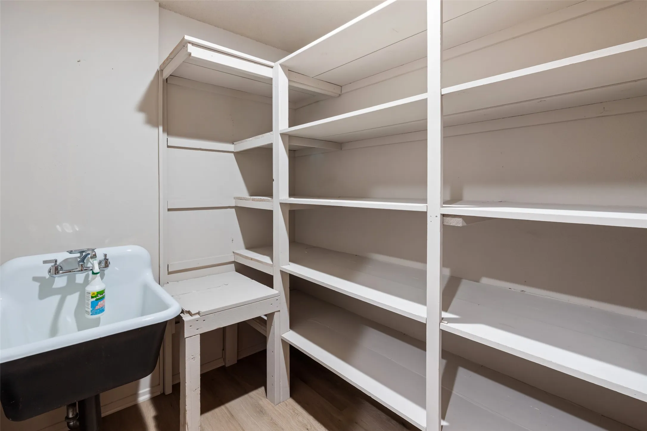 Utility room featuring extensive built-in shelving, a white utility sink, and wood-finish flooring