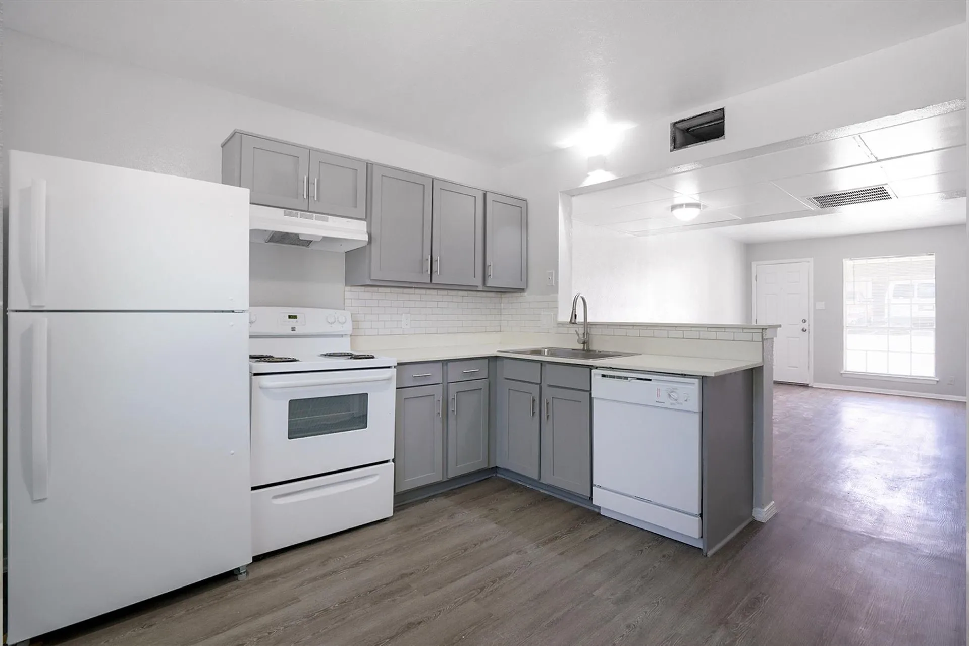 Contemporary kitchen featuring gray cabinetry, white appliances, light countertops, and subway tile backsplash