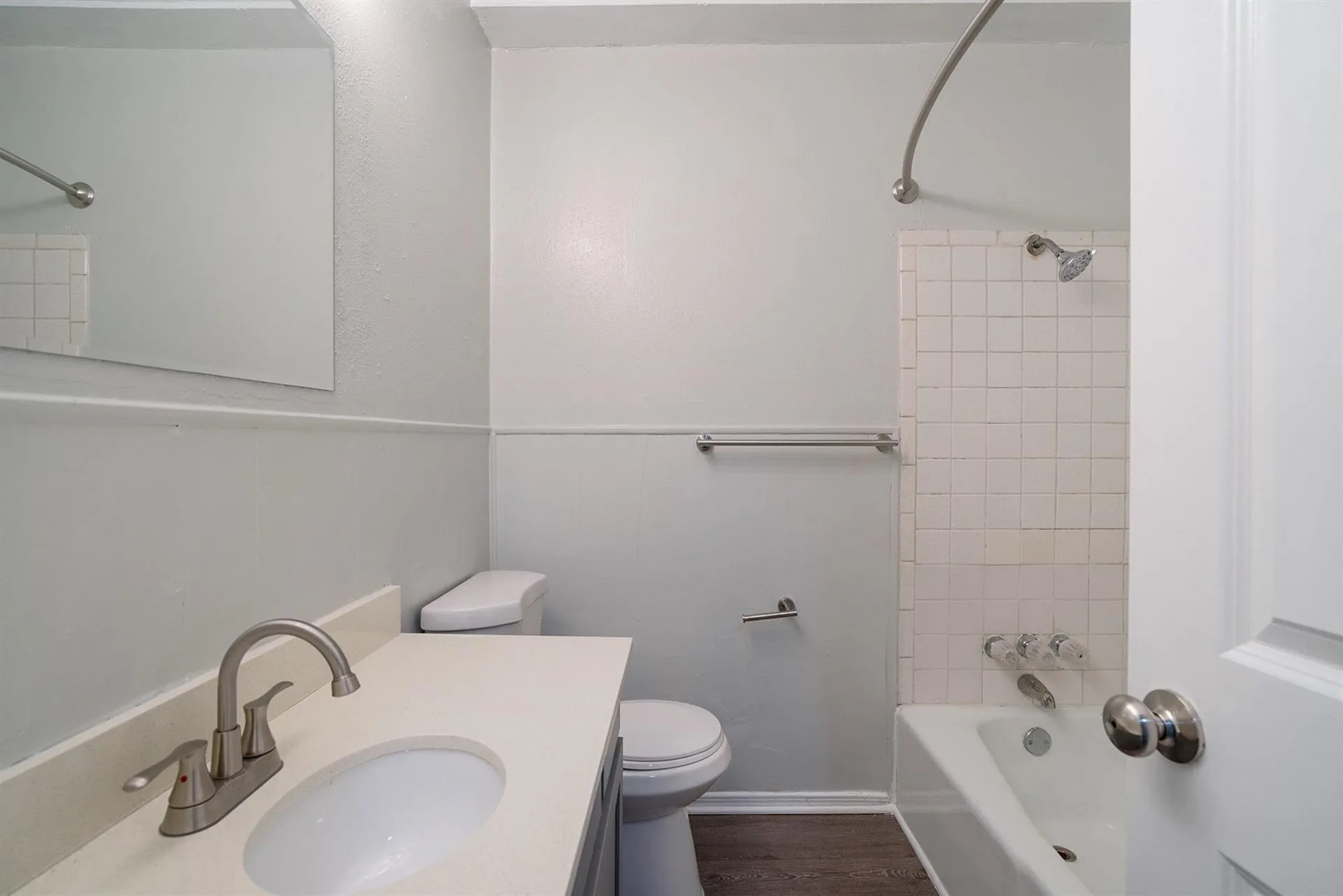 Bathroom featuring a vanity with an integrated sink and brushed nickel faucet, a toilet, and a combination tub/shower with white tile surround