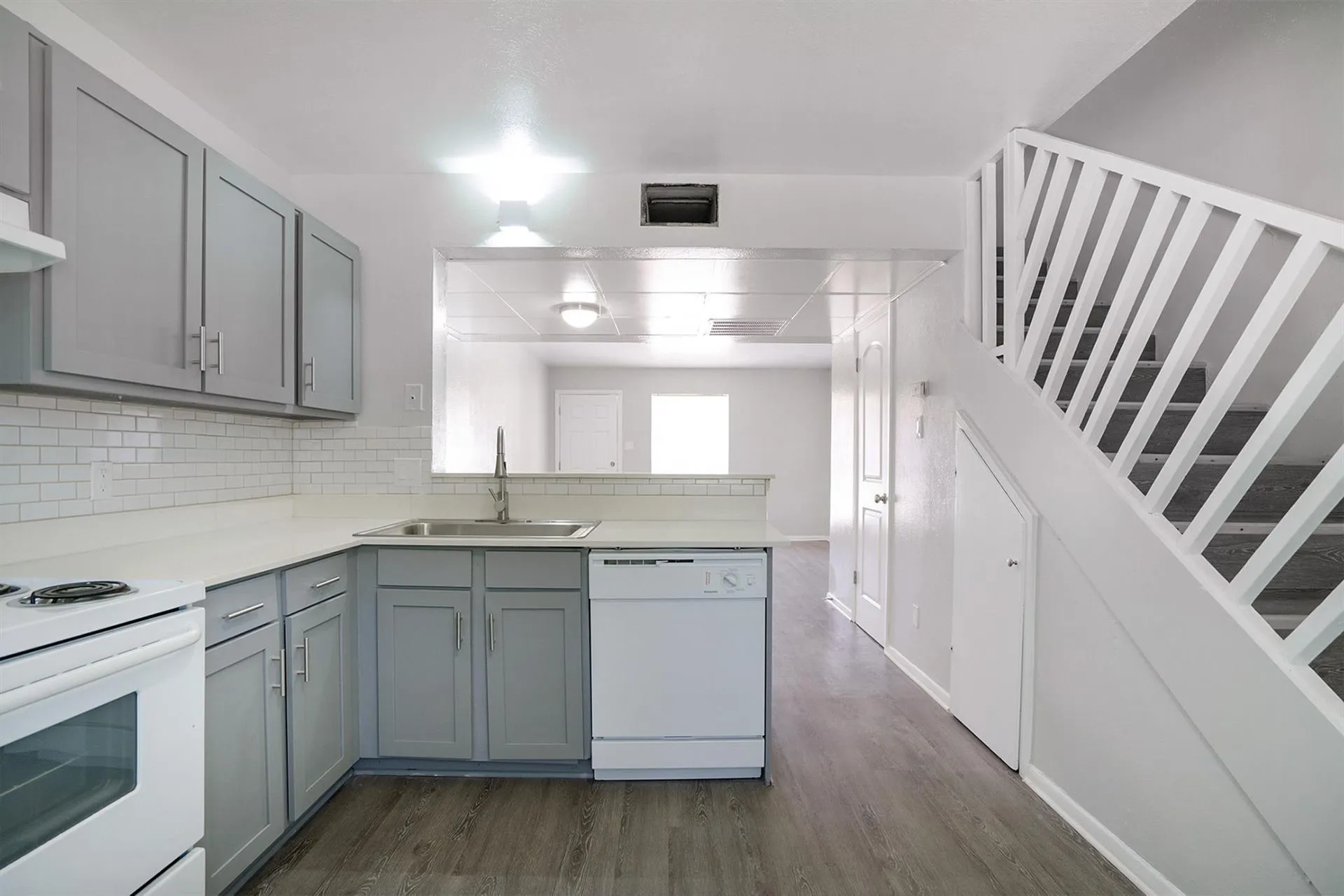 Kitchen featuring grey cabinetry with silver hardware, white subway tile backsplash, light-toned countertops, and wood-finish flooring
