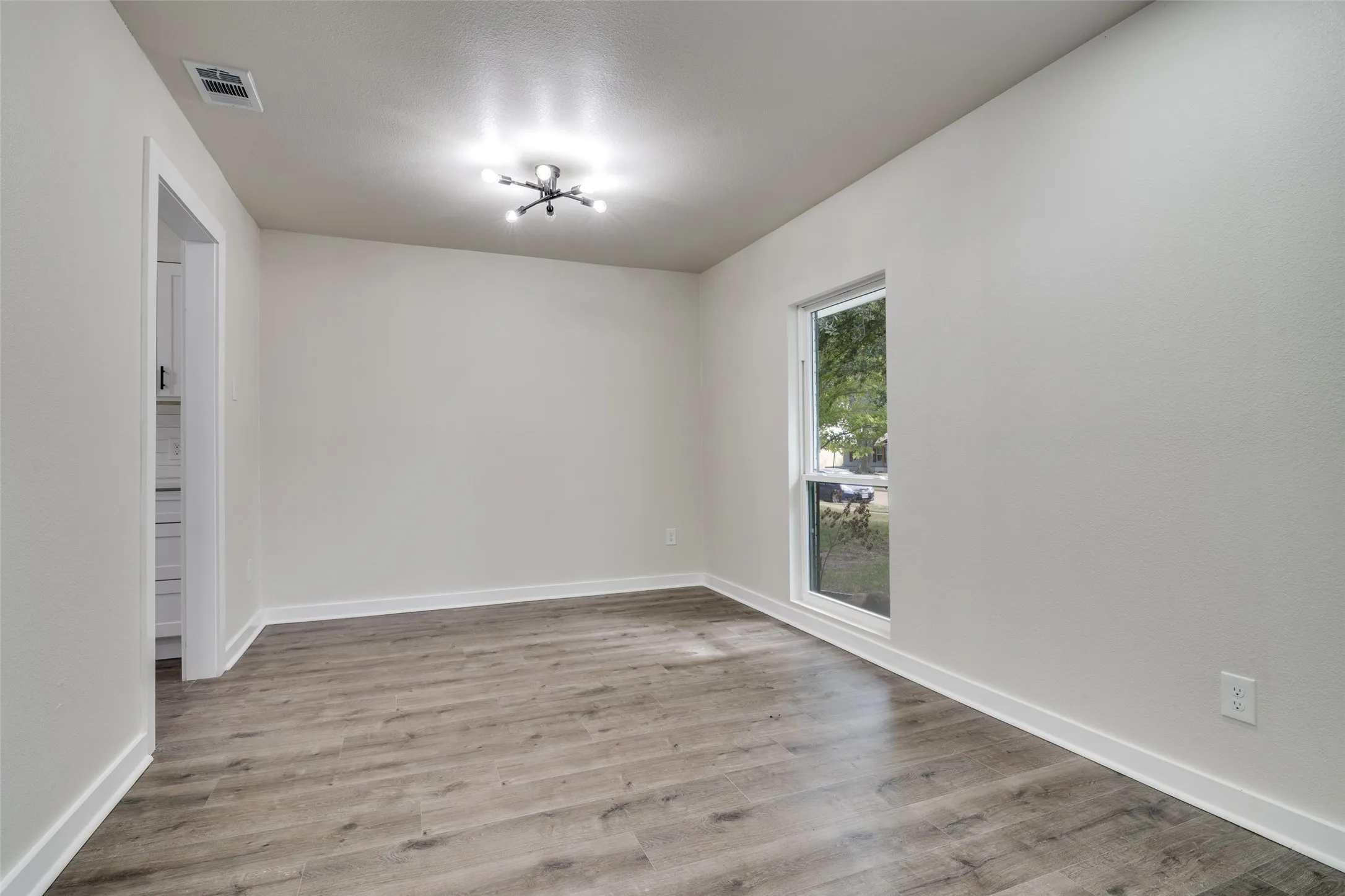 Spacious room featuring wood-finish flooring, white baseboards, and neutral wall tones