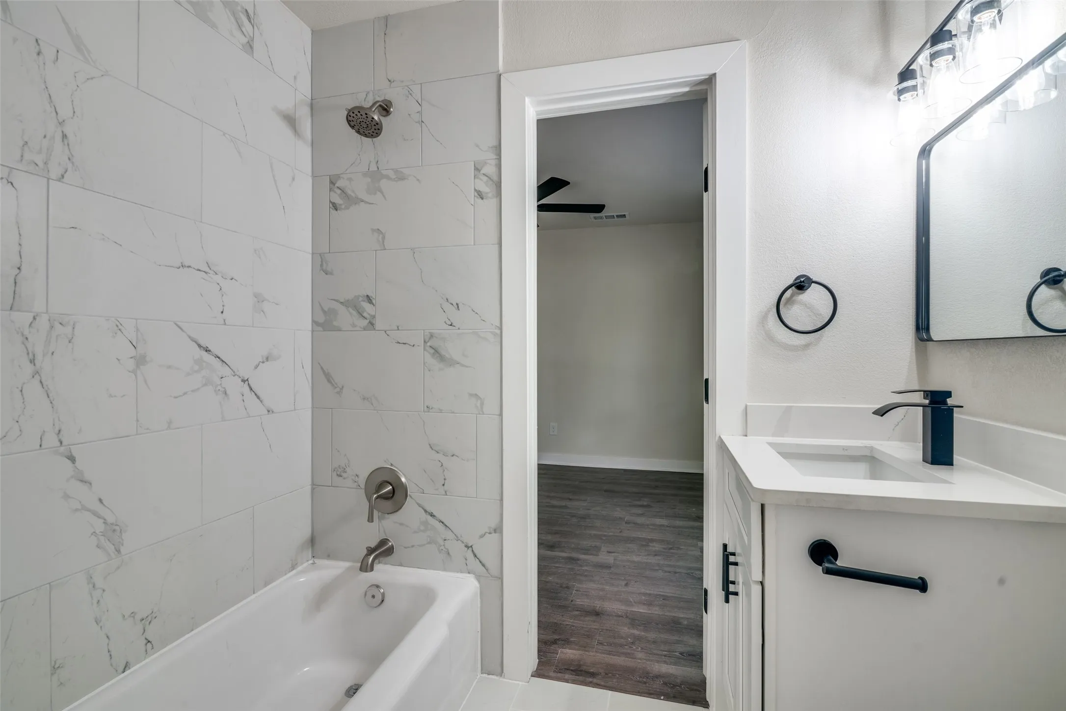 Bathroom featuring a white subway tile shower surround with subtle gray veining, a deep soaking tub with brushed nickel fixtures, and a modern vanity with a white countertop and integrated sink