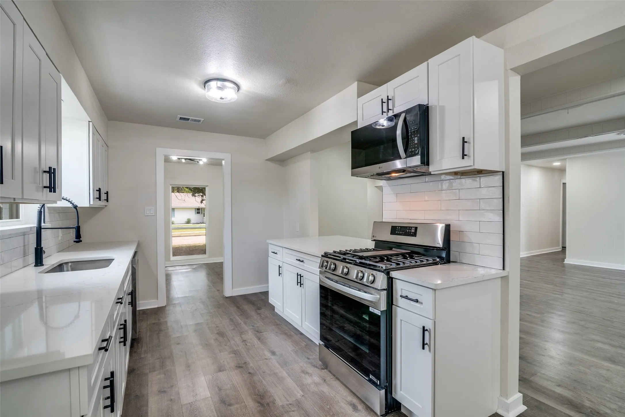 Kitchen featuring white shaker cabinetry, stainless steel appliances, quartz countertops, a subway tile backsplash, and wood-finish flooring