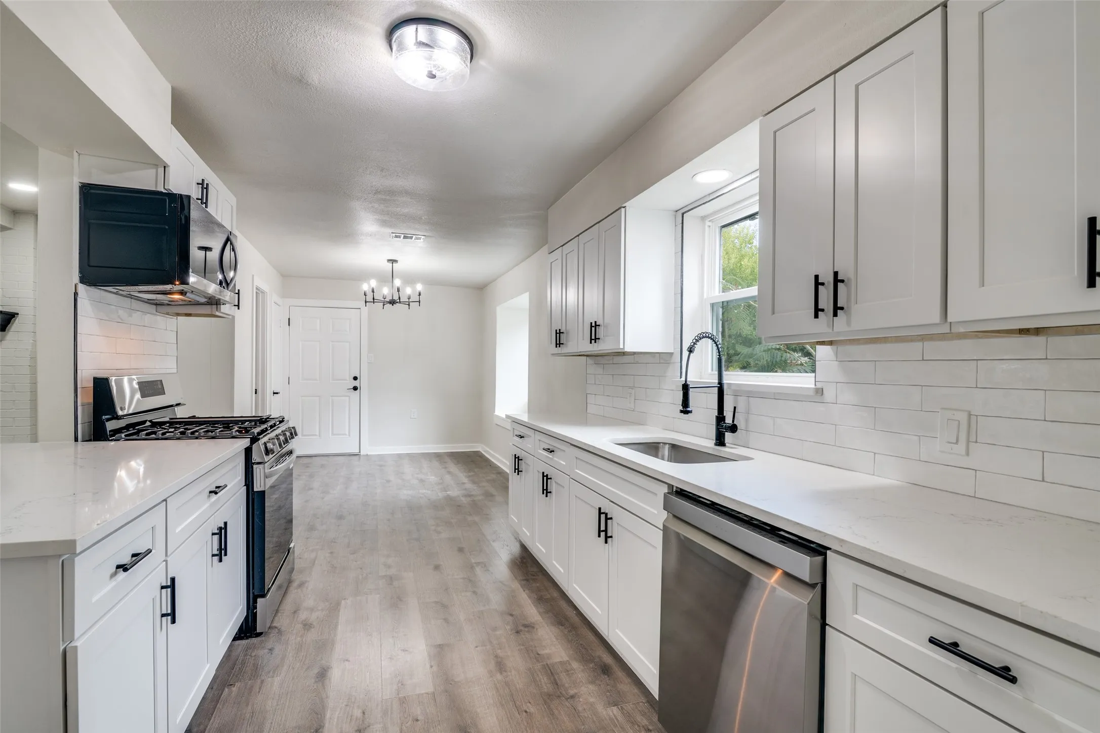 Bright kitchen showcasing white shaker cabinetry, stainless steel appliances, a window above the sink, light countertops, and wood-finish flooring