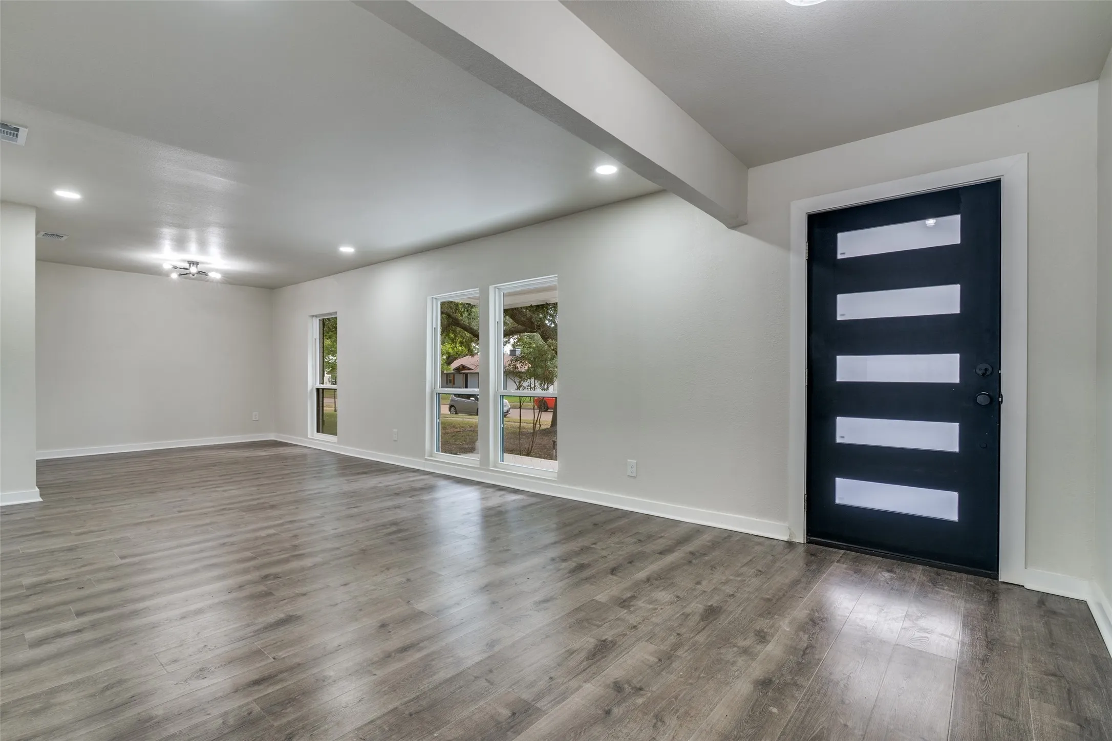 Spacious interior featuring wood-finish flooring, recessed lighting, and a contemporary black entry door with frosted glass inserts