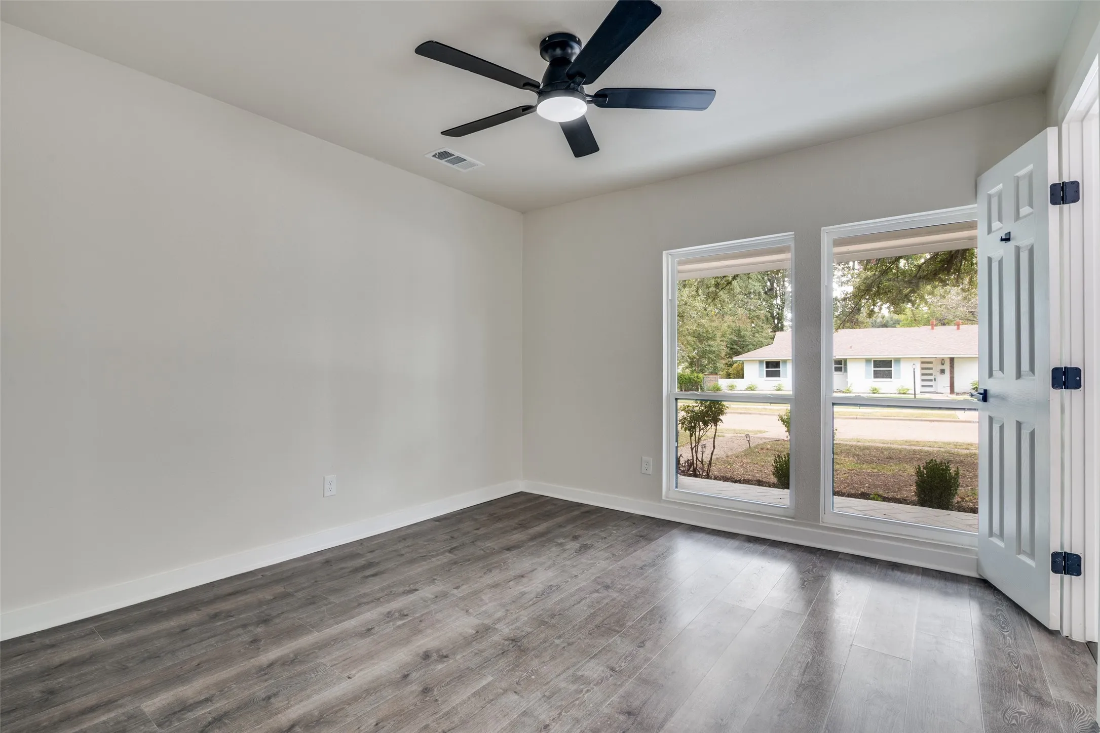 Interior room featuring wood-finish flooring, two large windows, a ceiling fan with integrated lighting, and white baseboards