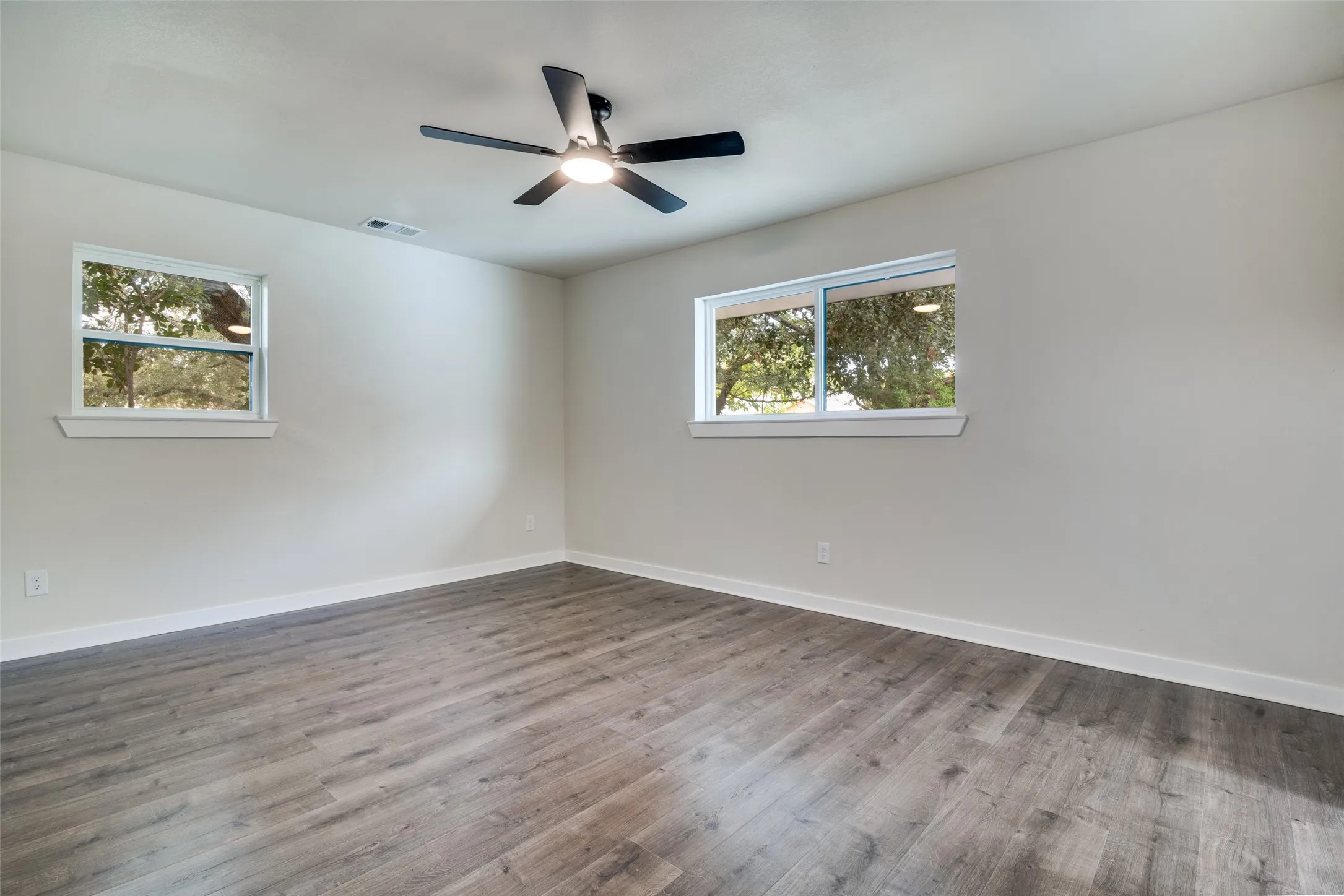 Spacious room featuring wood-finish flooring, light gray walls, and white baseboards