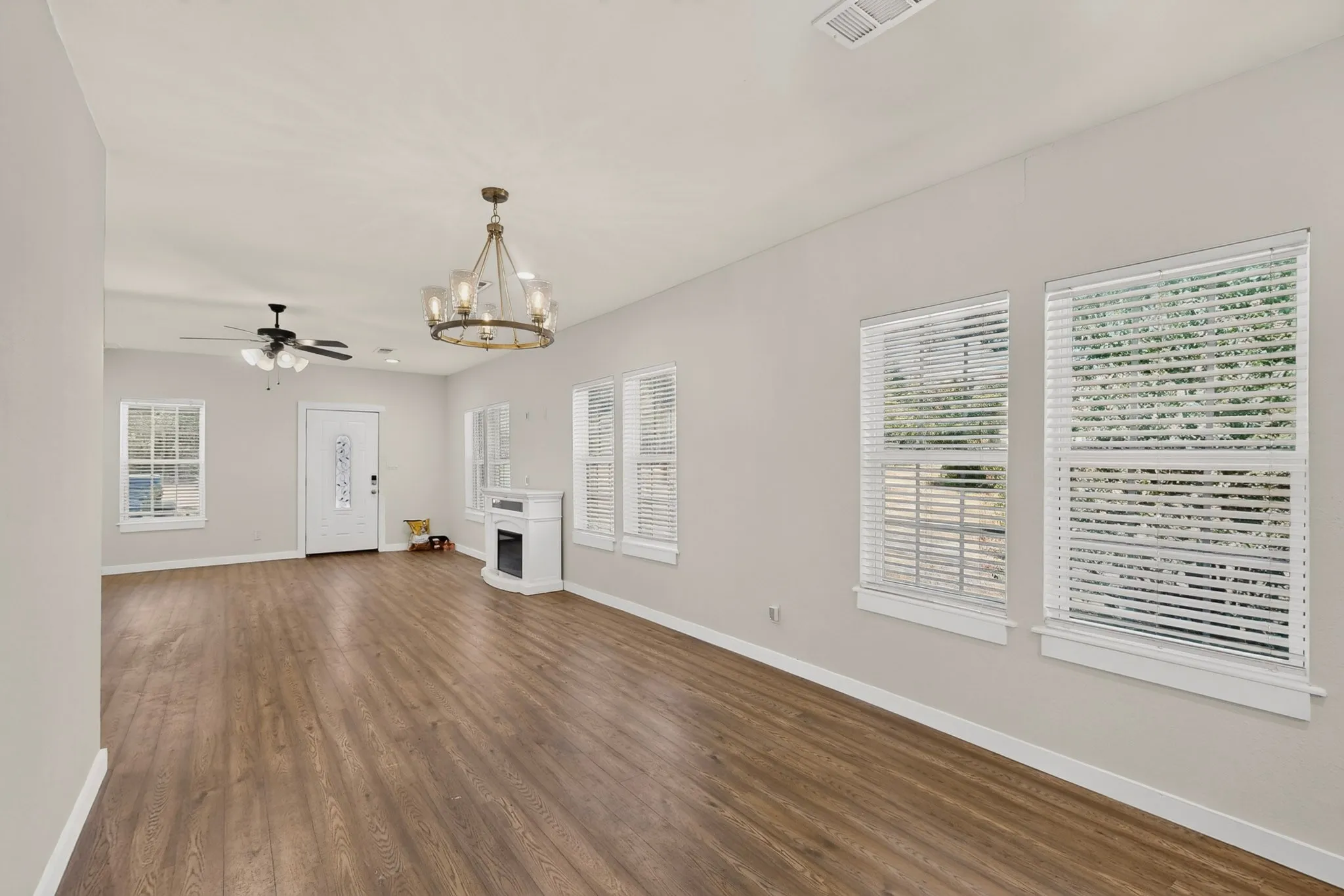 Wood-finish flooring throughout, multiple windows with blinds, ceiling fan, decorative fireplace, and a glass-paneled front door