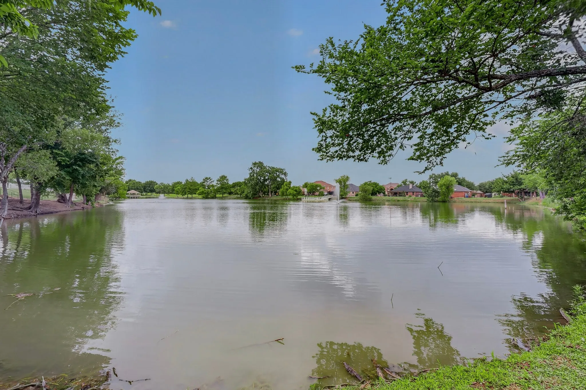 Expansive lakeside setting featuring mature trees, a tranquil water body, and a distant water feature