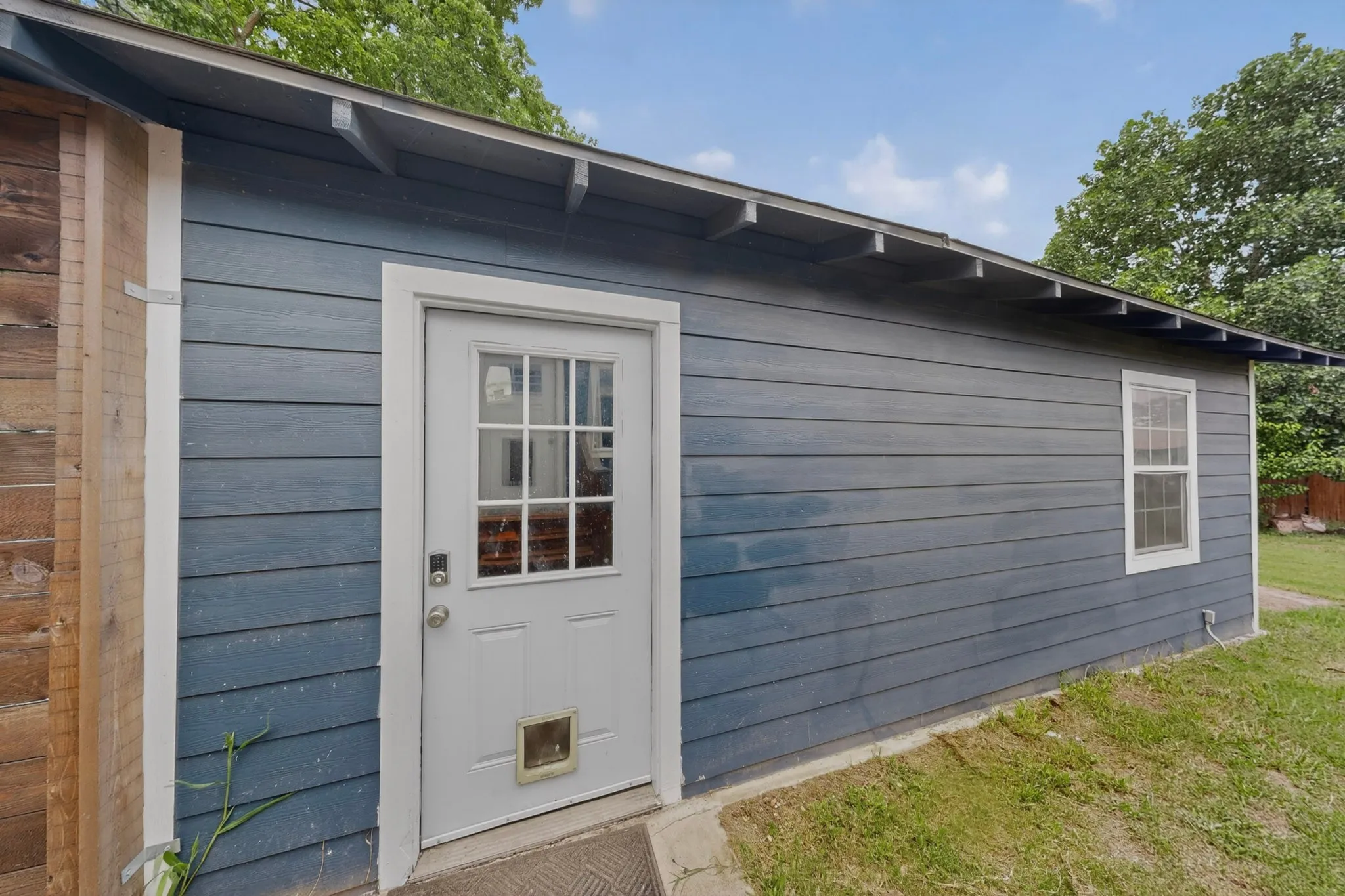 Exterior featuring dark blue horizontal siding, white-trimmed windows, a wooden privacy fence, and a wooden deck with stairs