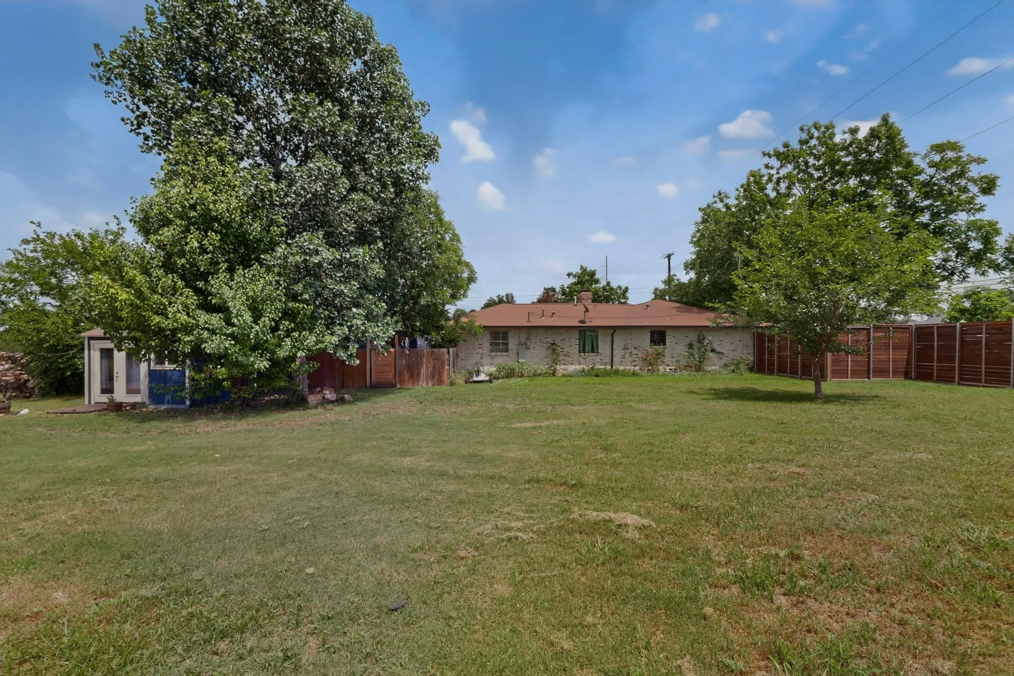 Expansive grassy yard area featuring a perimeter fence, mature trees, and raised garden beds