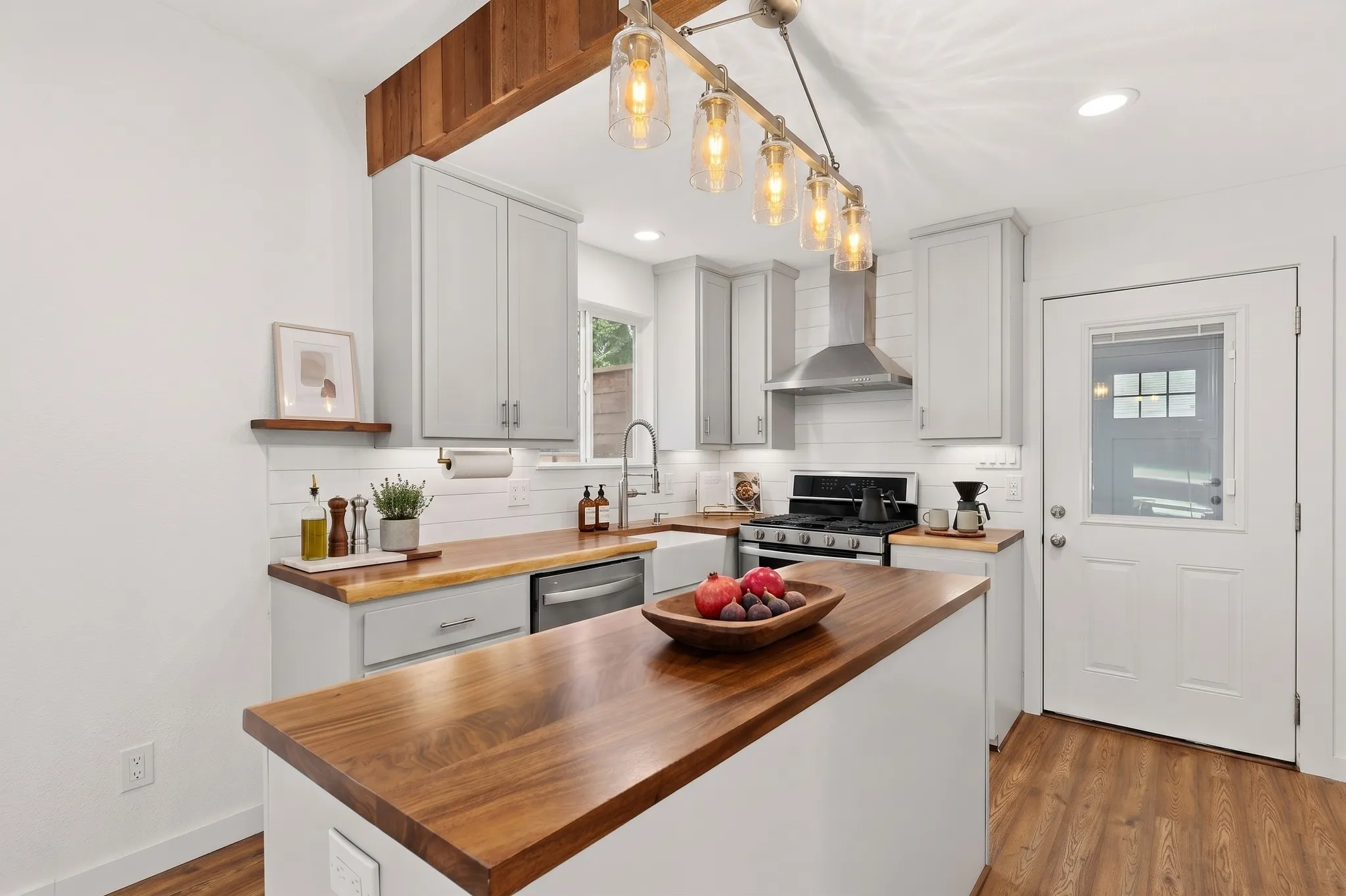 Kitchen featuring wood-finish flooring, a central island with a wood countertop, light gray cabinetry, and a white subway tile backsplash