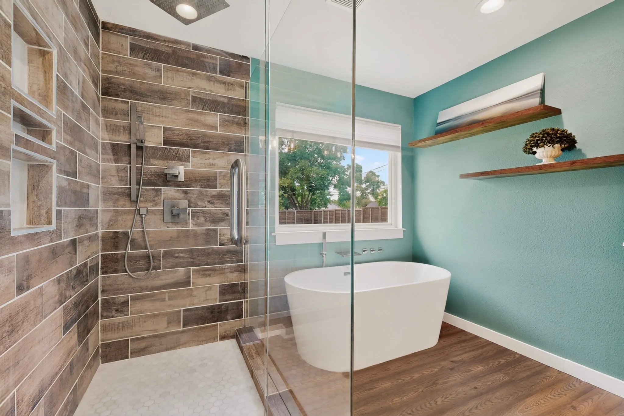 Bathroom featuring a freestanding tub, a walk-in glass shower with stone-look tile, wood-finish flooring, and a large window