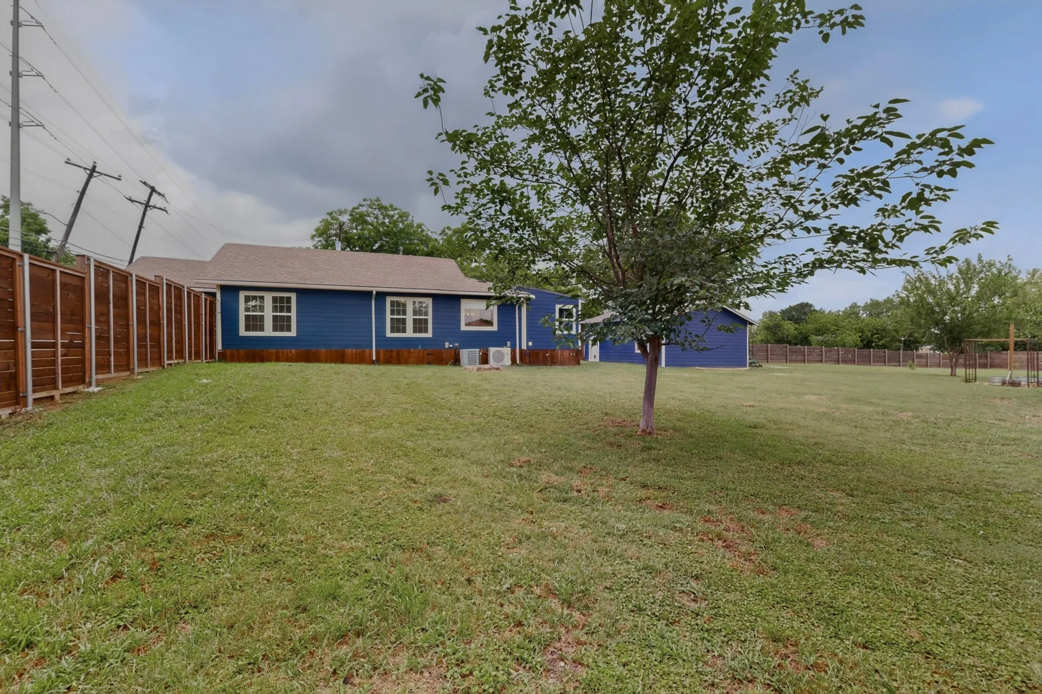 Expansive grassy yard encompassing the rear of the property, featuring a privacy fence, exterior siding, and a detached structure