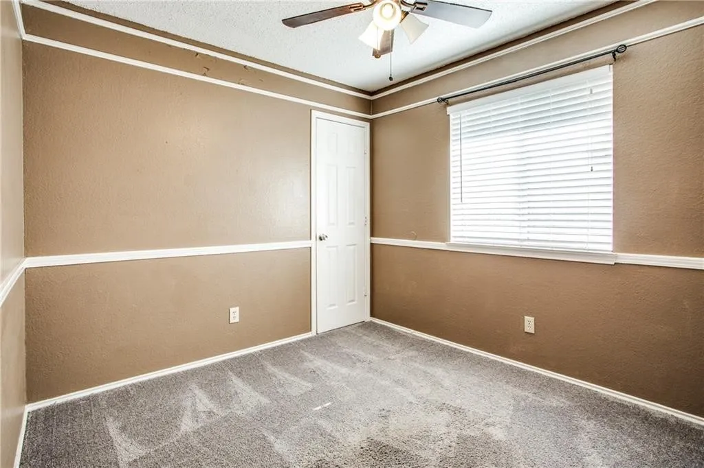 Carpeted room featuring a ceiling fan with integrated lighting, a window with blinds, and a white paneled door