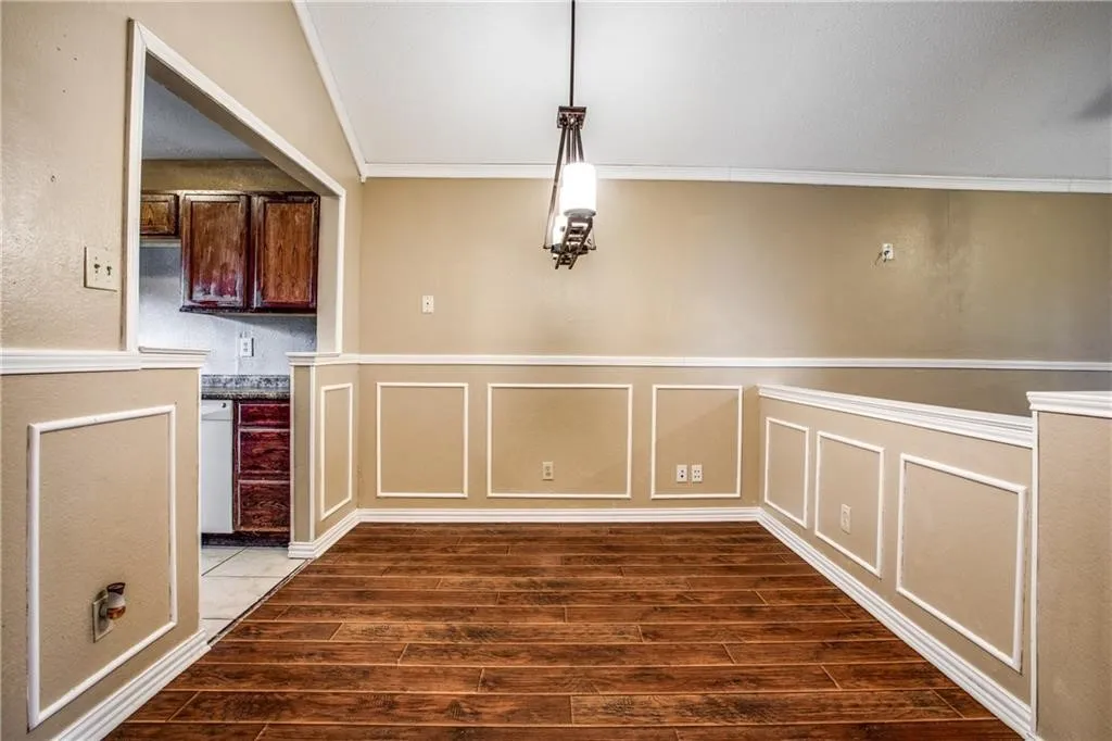 Dining area featuring wood-finish flooring, wainscoting, crown molding, and a decorative chandelier