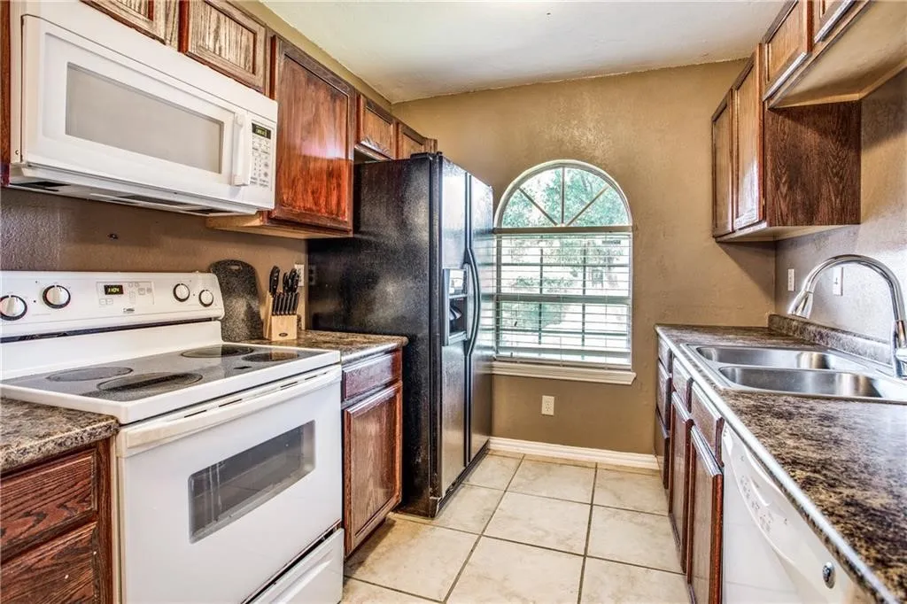 Kitchen featuring wood cabinetry, speckled countertops, white appliances, and a double basin stainless steel sink