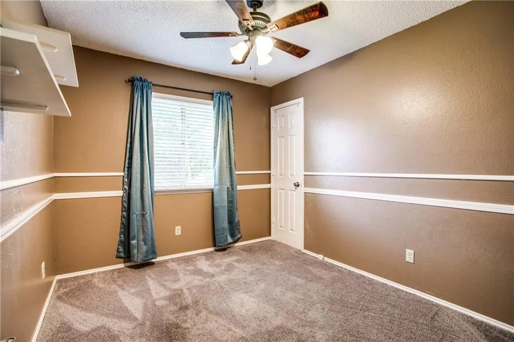 Carpeted room featuring a ceiling fan with light fixture, window with blinds, and white trim molding