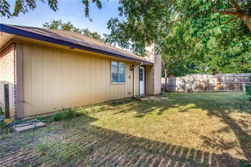 Rear exterior with a wood privacy fence, mature trees, and an exterior door