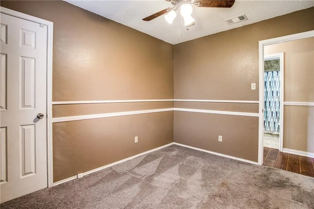 Bedroom featuring neutral-toned walls with chair rail molding, carpet flooring, a ceiling fan, and a paneled door