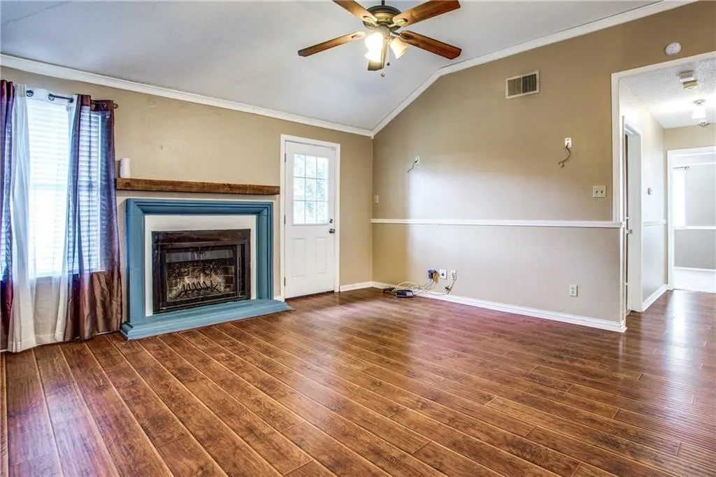 Living area featuring wood-finish flooring, a fireplace with a decorative mantel, and vaulted ceilings