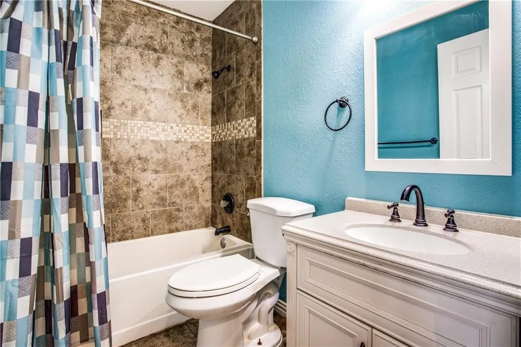Bathroom featuring a white vanity with an undermount sink and a light-toned countertop, dark-finished hardware, a framed mirror, and a shower/tub combination with tiled surround and decorative accent band
