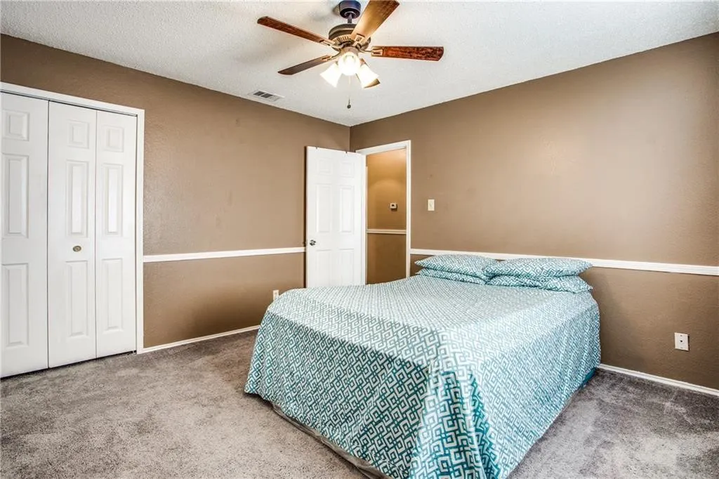 Carpeted room featuring a ceiling fan with light fixture, neutral-toned walls with chair rail molding, and bi-fold closet doors