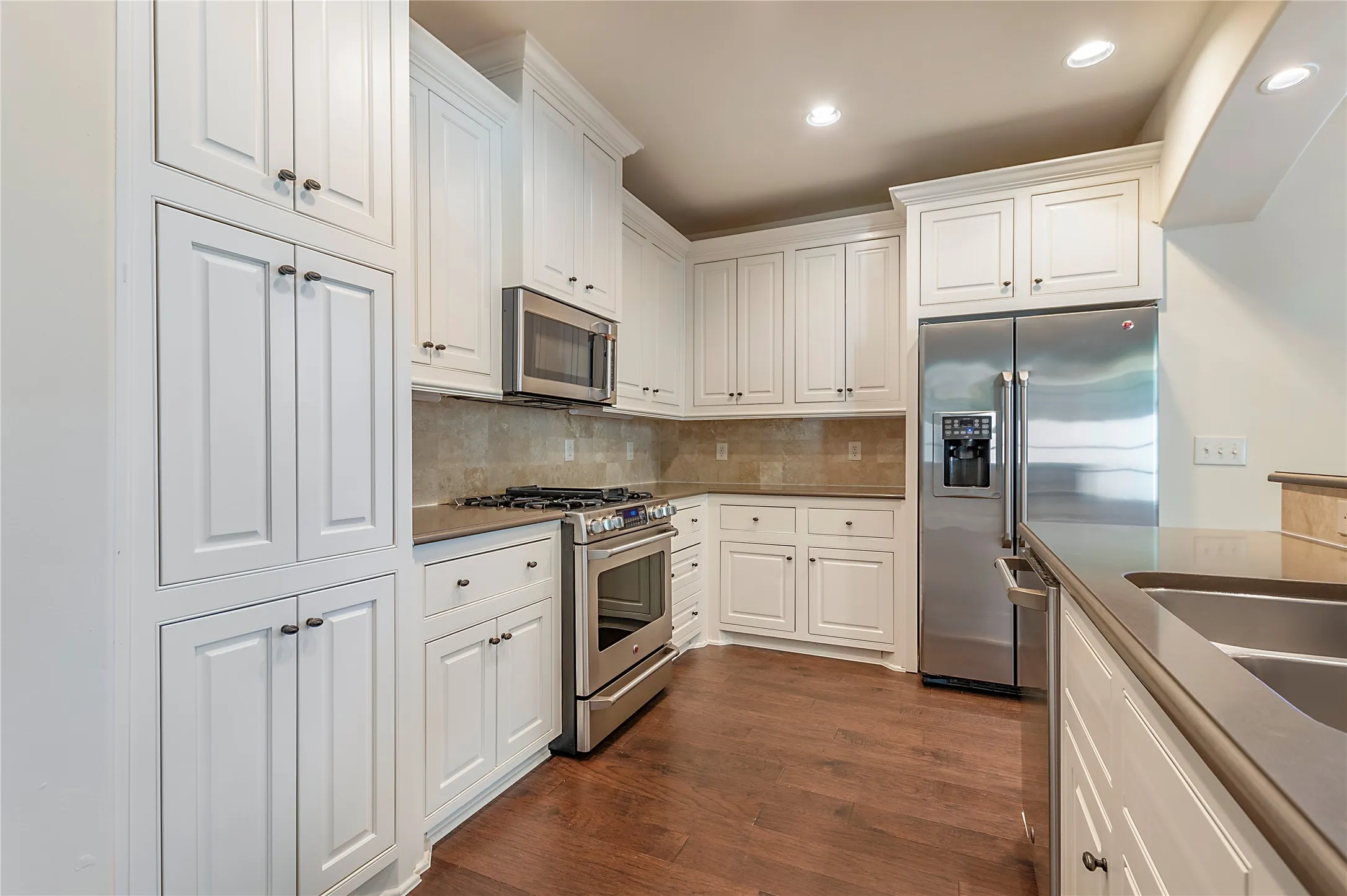 Kitchen with decorative backsplash, white cabinetry, dark hardwood / wood-style floors, and stainless steel appliances