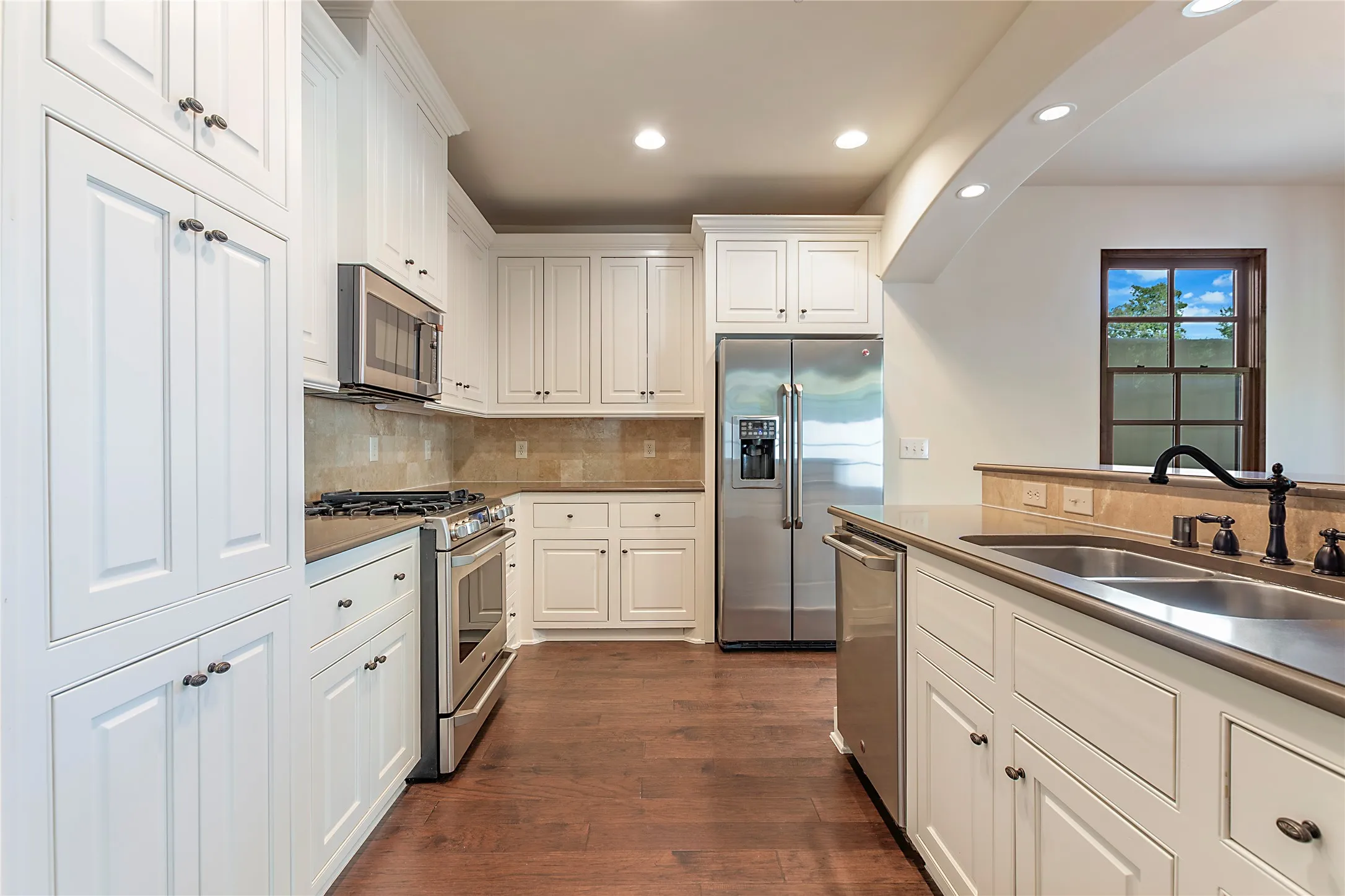 Kitchen with appliances with stainless steel finishes, decorative backsplash, white cabinets, dark hardwood / wood-style floors, and sink
