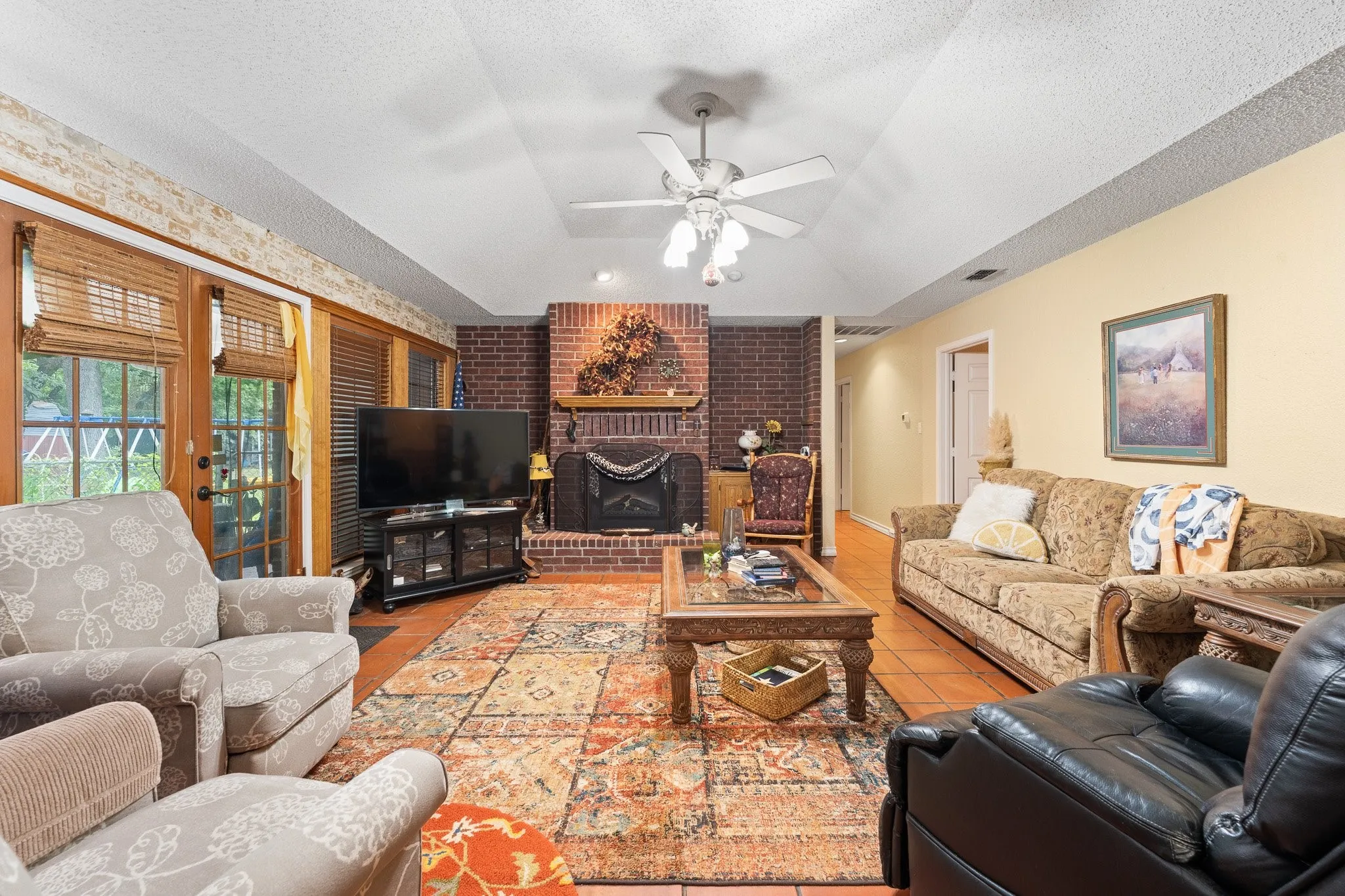 View of living room from the kitchen with wooden blinds, trey ceiling, french doors to backyard, and the cozy fireplace as the centerpiece