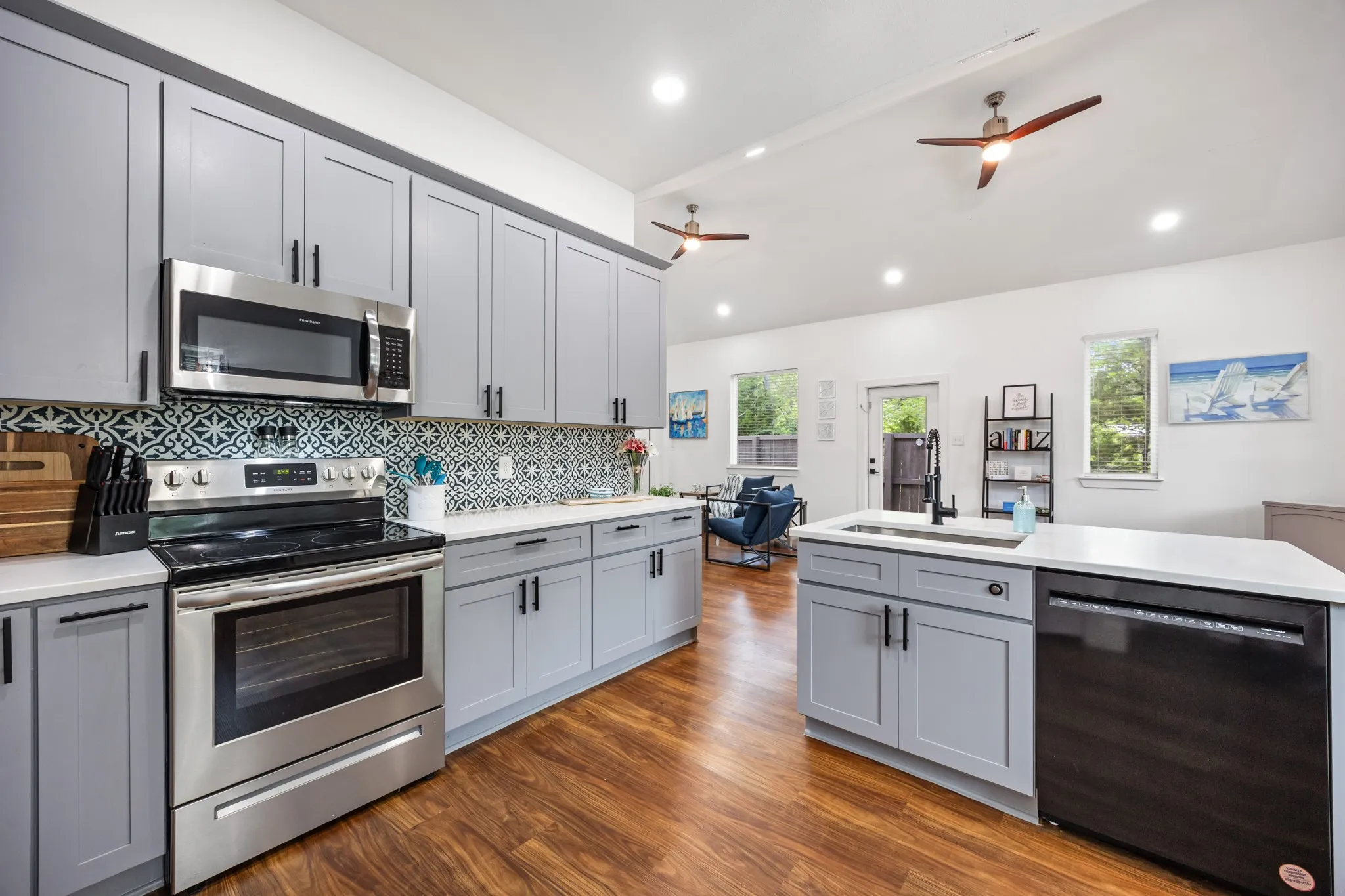 Modern kitchen featuring light gray cabinetry, stainless steel appliances, patterned tile backsplash, white countertops, and wood-finish flooring