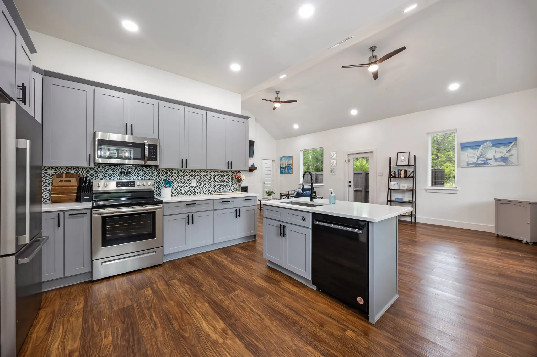 Spacious kitchen featuring an island with sink, stainless steel appliances, patterned tile backsplash, light gray cabinetry, and wood-finish flooring