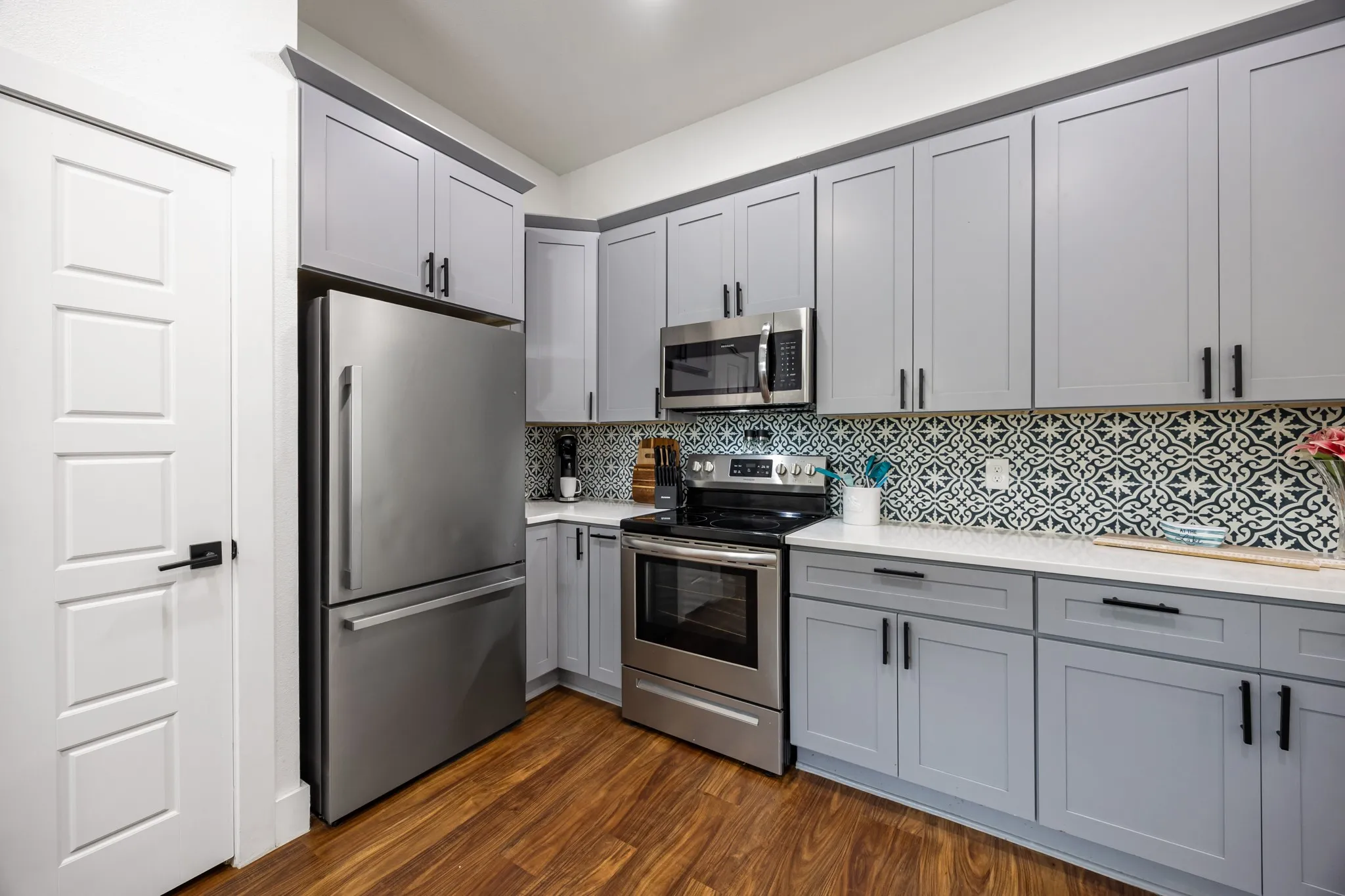 Modern kitchen with light gray cabinetry, stainless steel appliances, white countertops, and wood-finish flooring