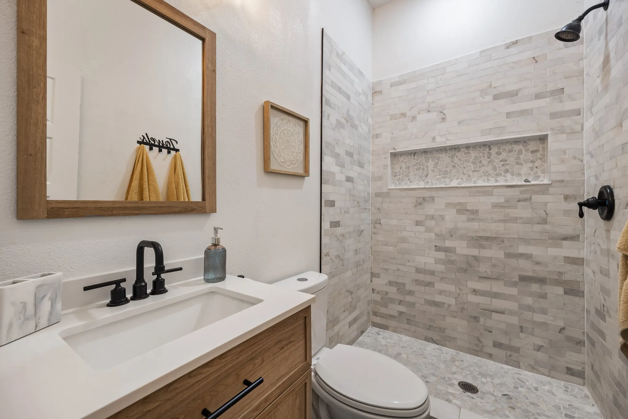 Bathroom featuring a wood-finish vanity with a white countertop and rectangular undermount sink, matte black faucet, and a framed mirror