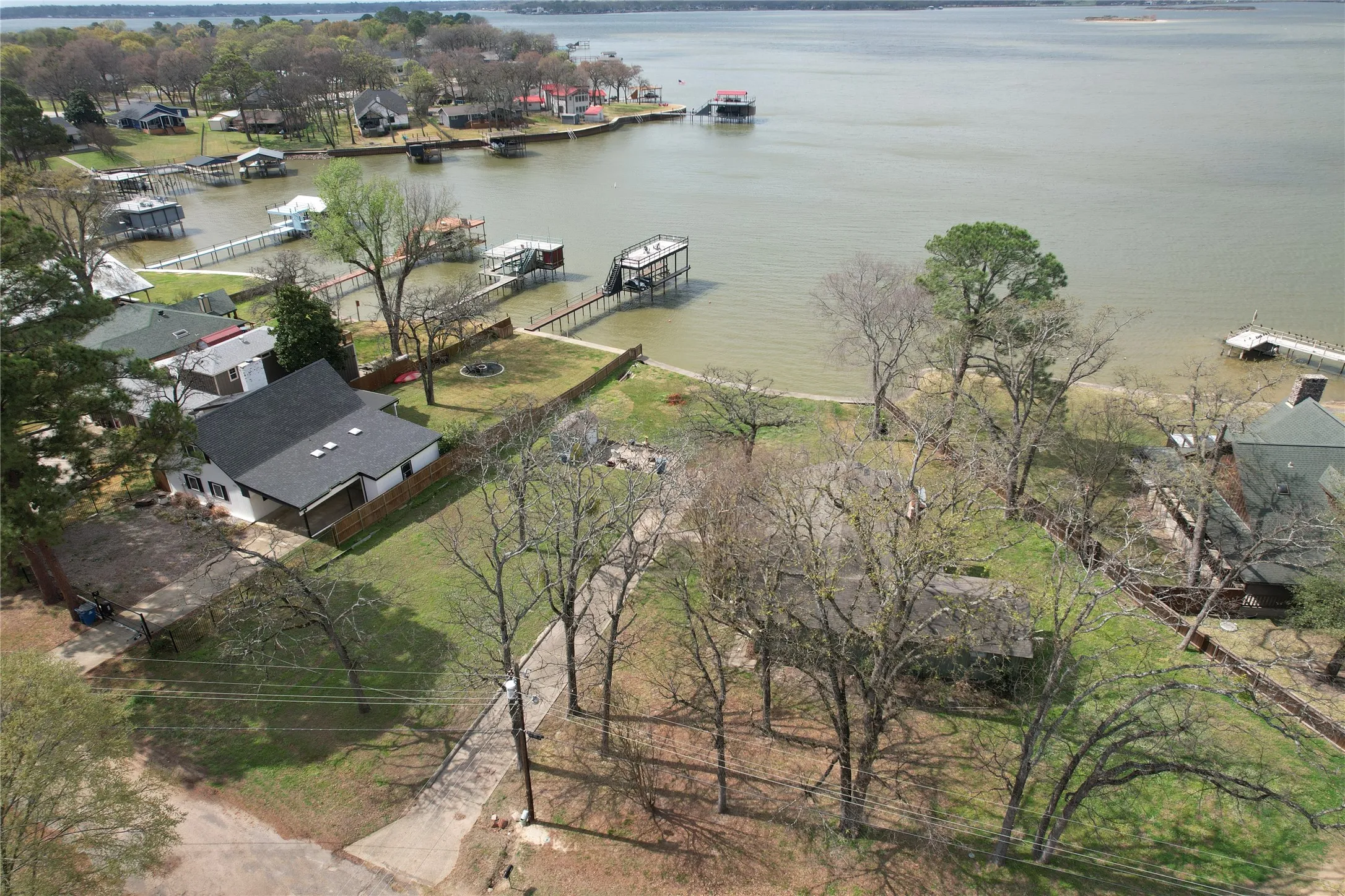 Lakefront property featuring a private boat dock, a gray shingle roof, a fenced backyard, and mature trees throughout the lot